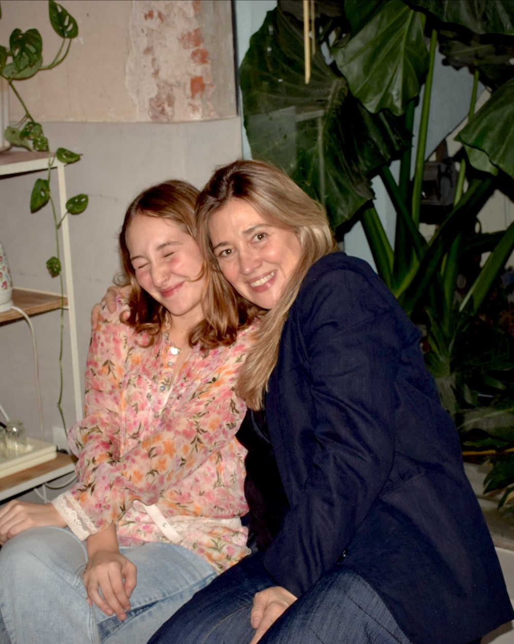 Joaquina y Alejandra, hija y madre, abrazadas y riendo en el taller, entre plantas.