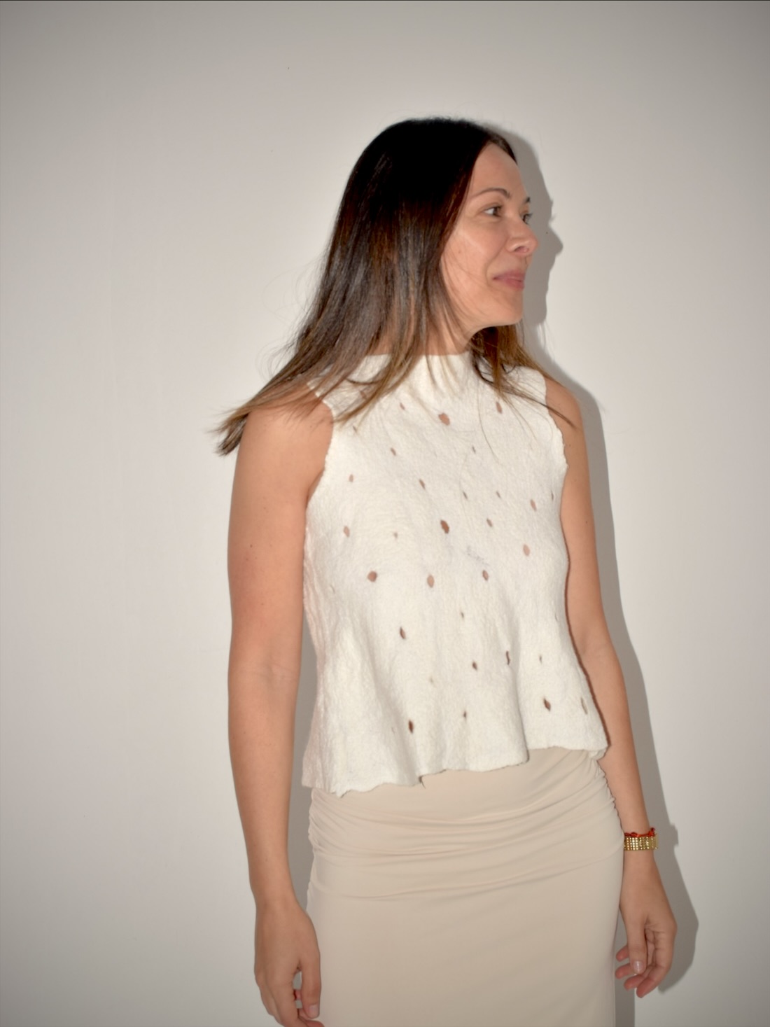 Mujer de perfil con una musculosa de nuno fieltro blanca, calada con pequeños óvalos, sobre una falda larga lisa color arena.