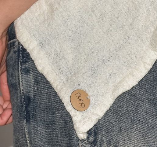 Etiqueta redonda de cuero con el nombre nuno, cosida en la punta de una prenda marfil.