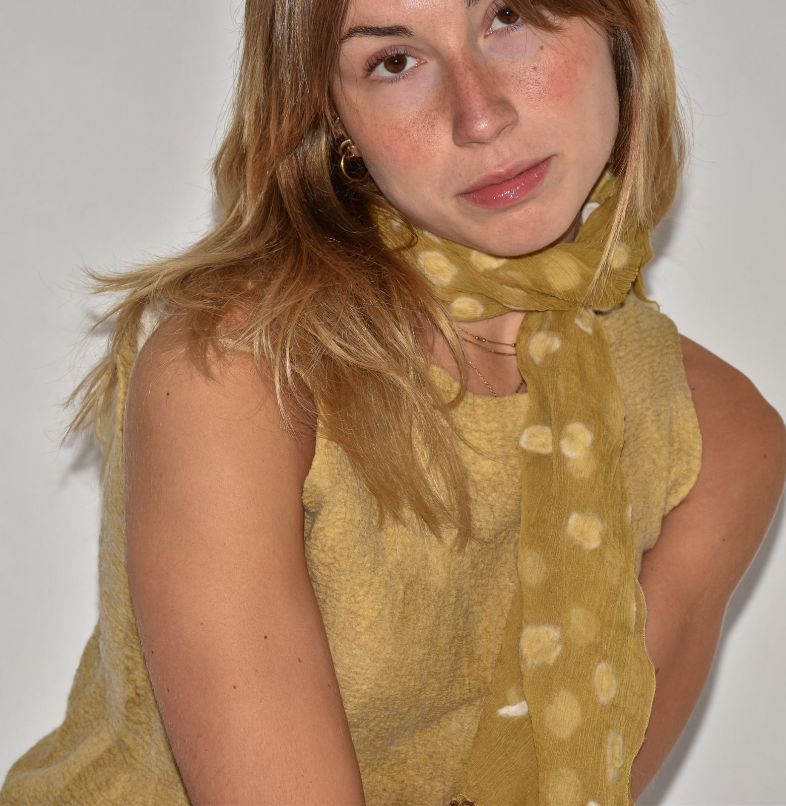 Musculosa de nuno fieltro color mostaza con relieve burbujeante, llevada con una bufanda de seda del mismo tono con lunares claros.